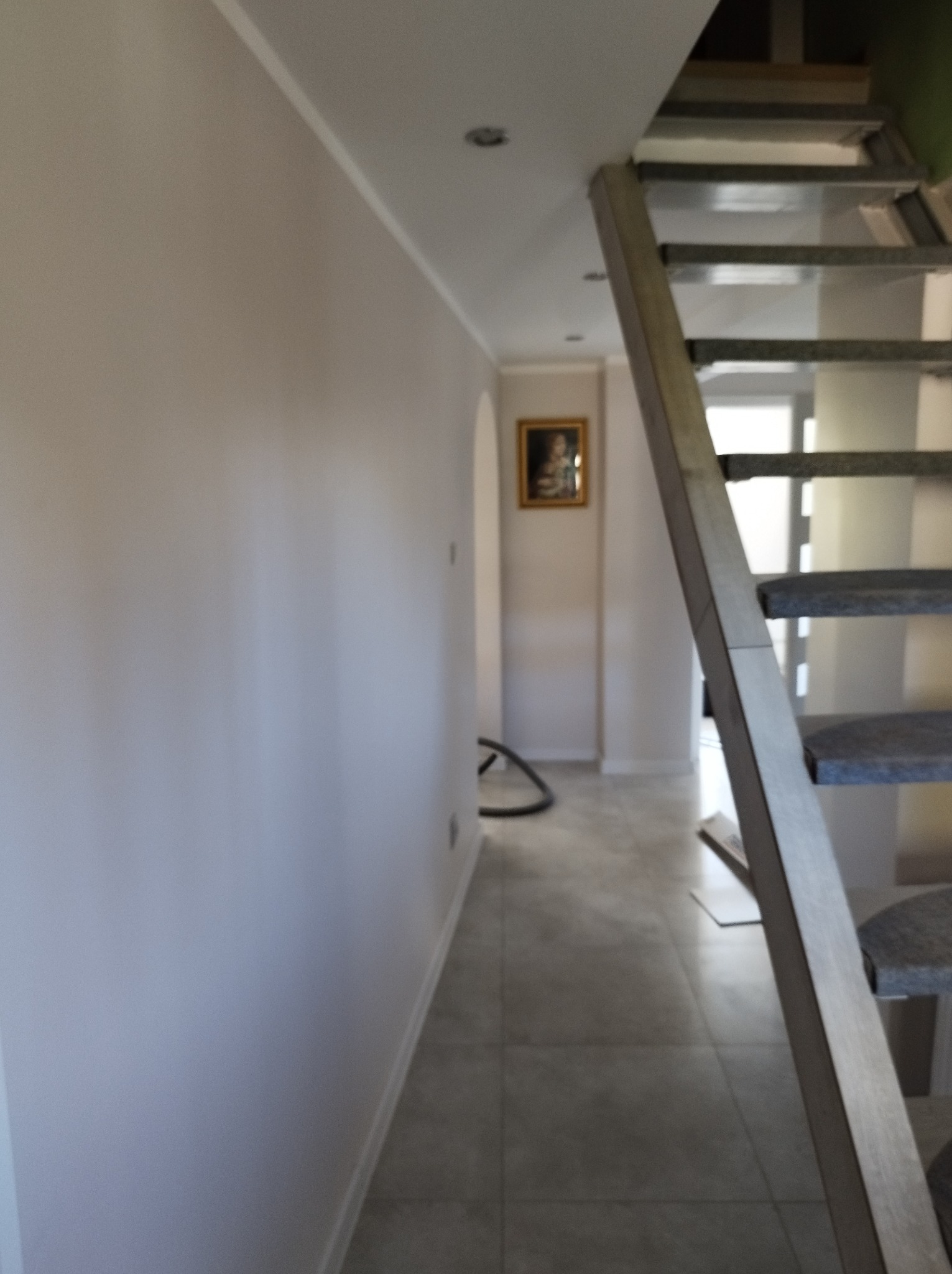 Jasna ściana po malowaniu, widoczne schody z metalowymi stopniami i obraz w ramie w tle. Minimalistyczne wnętrze po remoncie, neutralna kolorystyka.