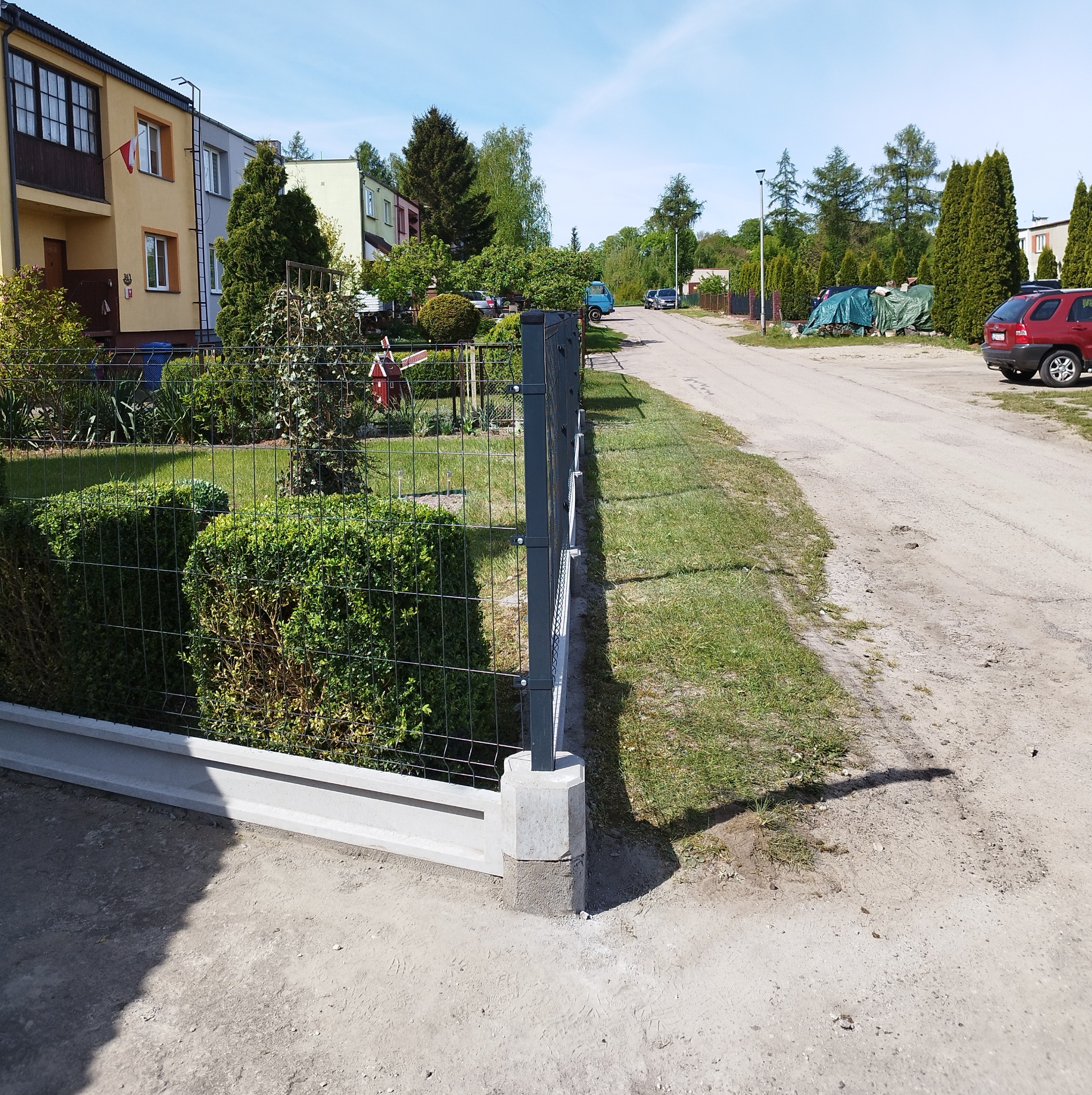 Nowoczesne ogrodzenie panelowe z podmurówką betonową, widok z zewnątrz posesji, zieleń w tle, słoneczny dzień.