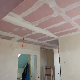 Montaż sufitu podwieszanego z płyt kartonowo-gipsowych, widoczne szpachlowane łączenia i kable elektryczne zwisające z sufitu.