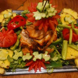 Dekoracyjnie podane danie z grillowanego kurczaka, ananasa, ogórka i pomidorów na srebrnej tacy.