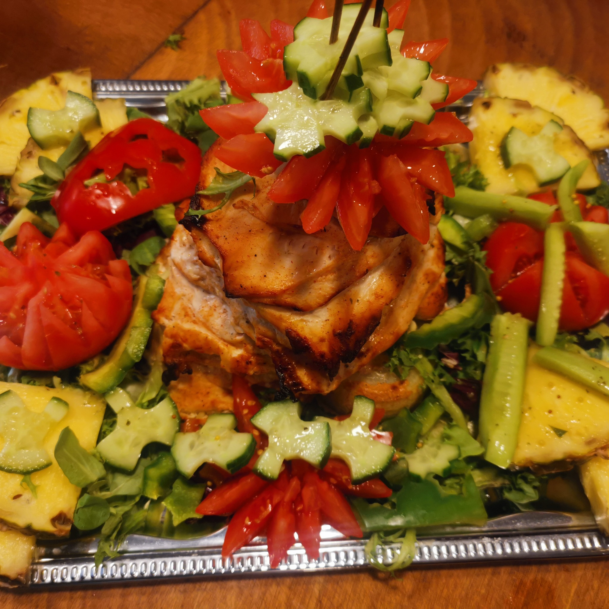 Dekoracyjnie podane danie z grillowanego kurczaka, ananasa, ogórka i pomidorów na srebrnej tacy.