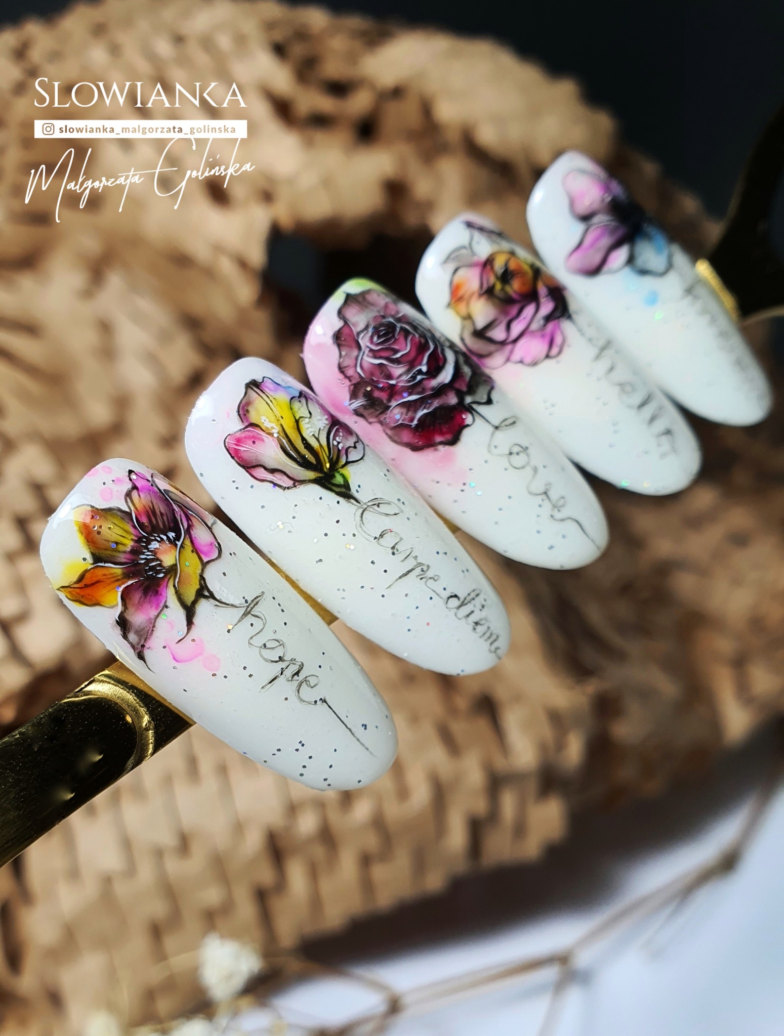 Delikatne, białe paznokcie w Bochni zdobione ręcznie malowanymi kwiatami i napisami 'Hope', 'Carpe diem', 'Love', prezentowane na złotym uchwycie i tle z naturalnego materiału.