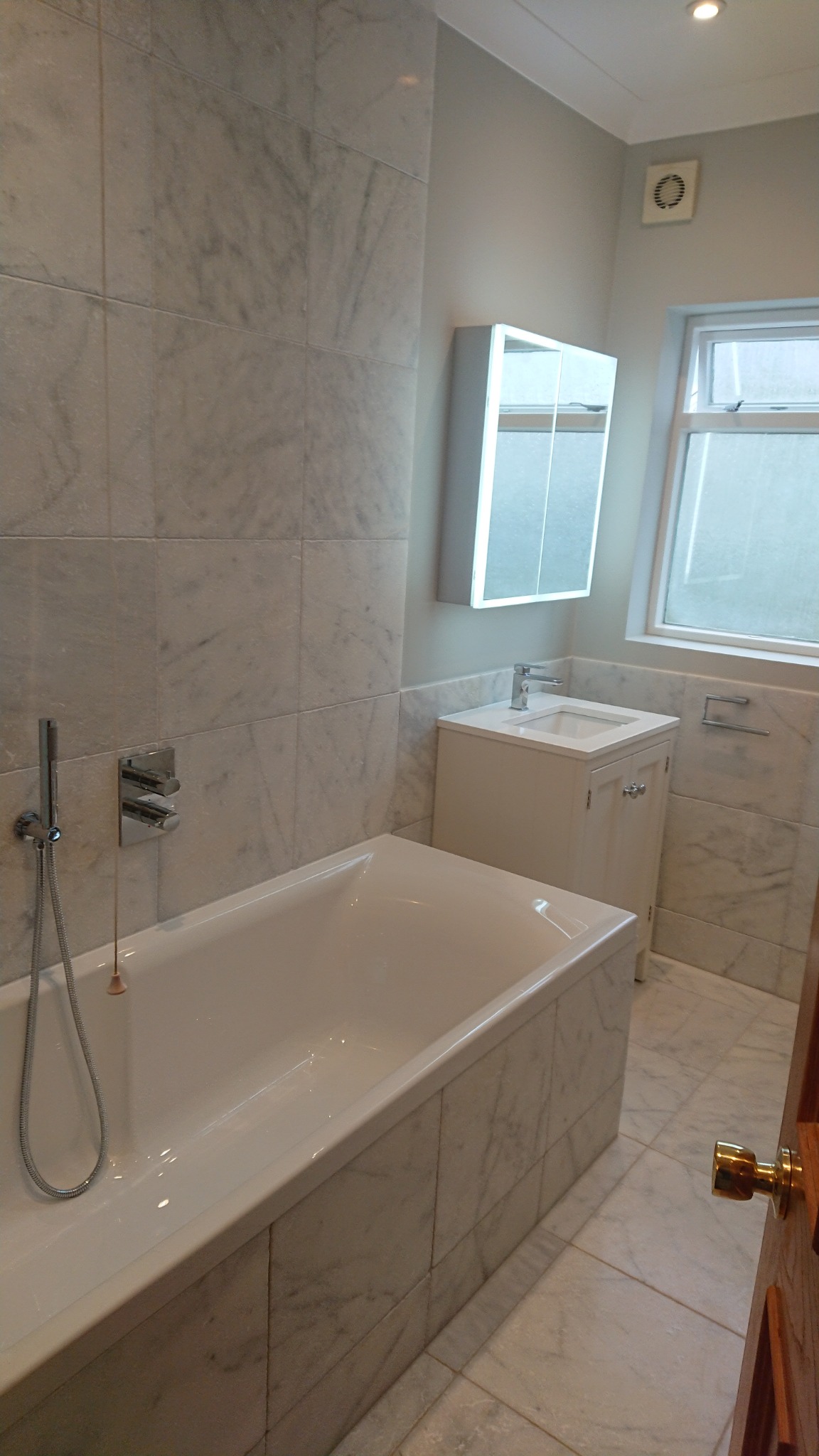 Wykończona łazienka z wanną obudowaną marmurowymi płytkami, umywalką z szafką i lustrem z podświetleniem LED.