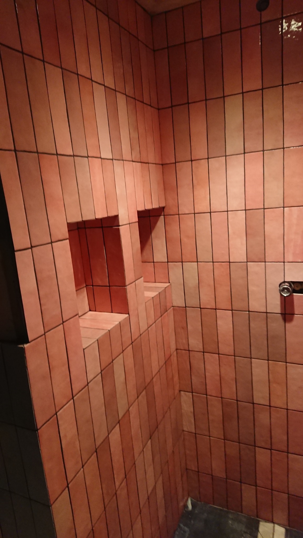 Wykończona łazienka z pionowo ułożonymi, podłużnymi, różowo-brązowymi płytkami i wnękami w ścianie na kosmetyki.