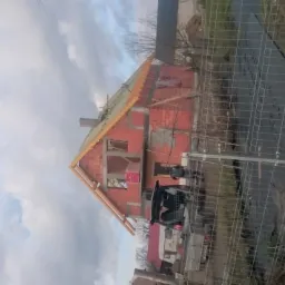 Budowa domu jednorodzinnego w trakcie realizacji, widoczna surowa konstrukcja dachu z drewnianymi elementami, ściany z czerwonej cegły, w tle pochmurne niebo.