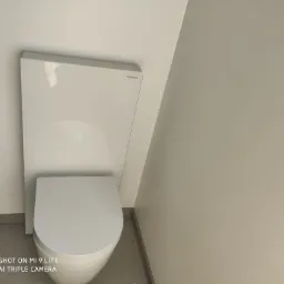 Nowoczesna, podwieszana toaleta Geberit z białą obudową, widoczna instalacja podtynkowa, minimalistyczne wnętrze łazienki w odcieniach bieli i szarości.