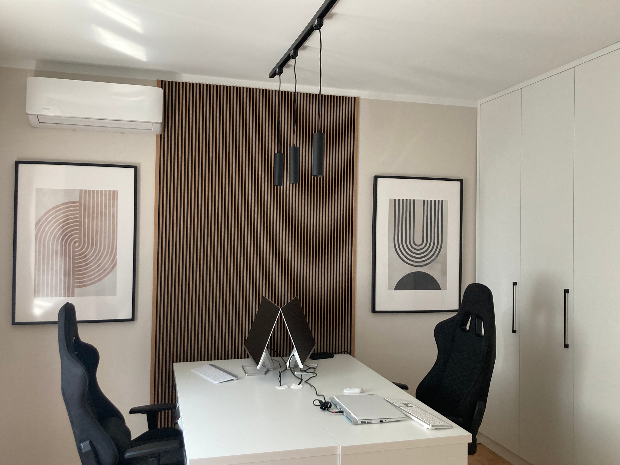 Nowoczesne biuro z dwoma stanowiskami pracy, minimalistycznym wystrojem, drewnianą ścianką działową, klimatyzacją i czarnymi krzesłami gamingowymi.