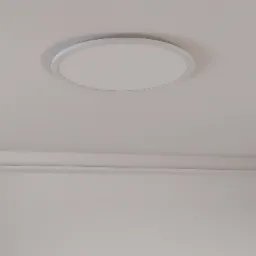 Zamontowany, okrągły, płaski panel LED w białej obudowie, wkomponowany w jasny sufit z subtelną listwą dekoracyjną przy ścianie.