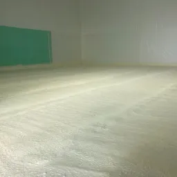 Wnętrze hali z wykonaną, jasną posadzką przemysłową o chropowatej fakturze, zabezpieczone folią ściany, fragment zielonej ściany w tle.