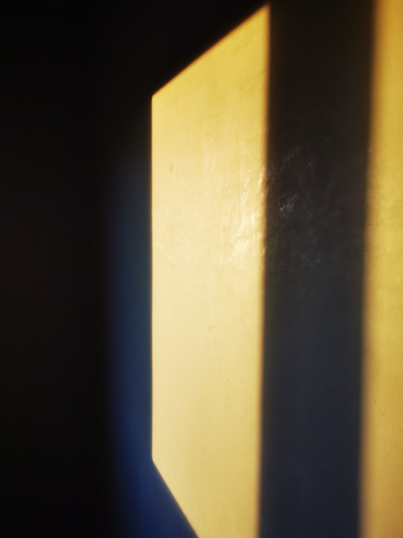 Fragment ściany z nałożonym tynkiem, oświetlony silnym, bocznym światłem tworzącym wyraźny cień.