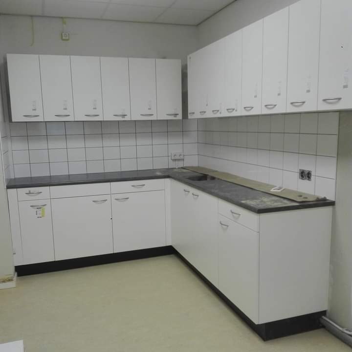 Wnętrze kuchni w trakcie remontu: białe szafki kuchenne górne i dolne z ciemnym blatem, białe płytki na ścianie, widoczne niedociągnięcia wykończeniowe.