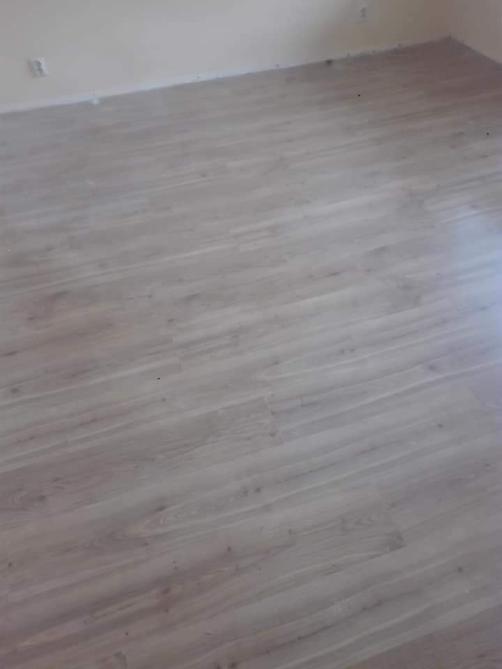 Jasne panele podłogowe ułożone w pustym pokoju z kremowymi ścianami, widoczne z perspektywy pod kątem.