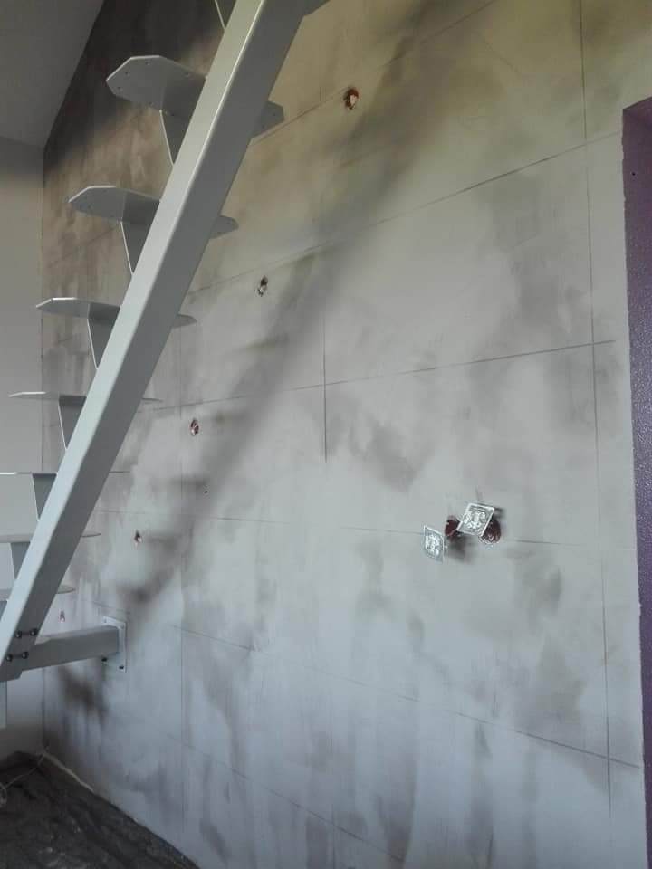 Ściana przygotowana pod płytki z zaznaczonymi liniami i wystającymi puszkami elektrycznymi, widoczne fragmenty metalowych schodów, Koszalin.