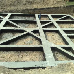 Siatka zbrojonego betonu tworząca fundament domu, widoczna w wykopie ziemnym, z niebieską szmatką na patyku w jednym z otworów.