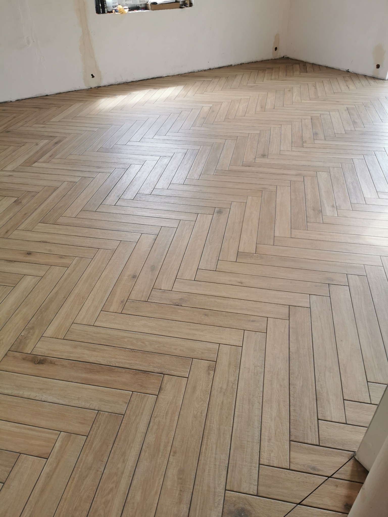 Ułożona parkietowa podłoga z jasnobrązowych płytek w jodełkę, widoczne niedokończone ściany w tle.