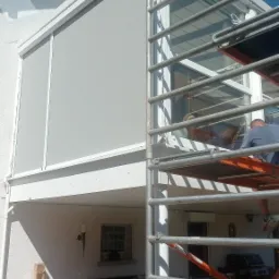 Montaż szarej żaluzji fasadowej na tarasie domu w Brzesku, widok z dołu na rusztowanie i częściowo zasłonięte okno.