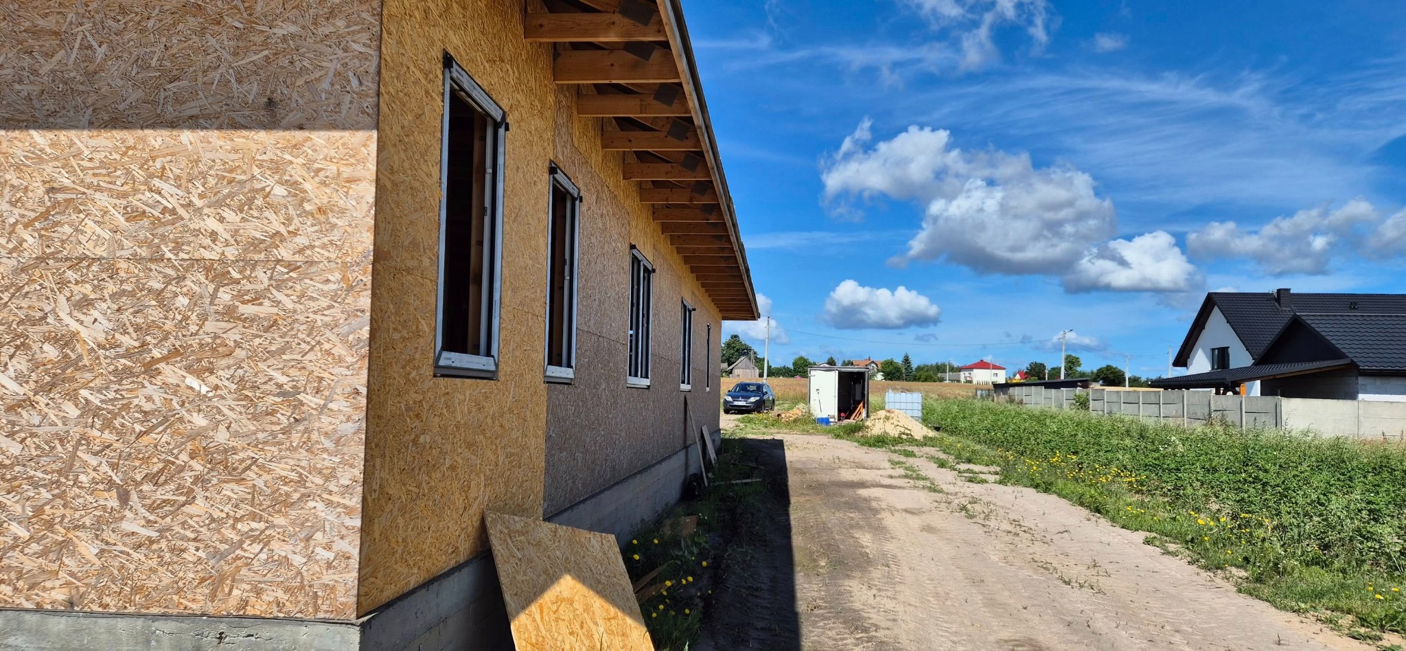Budowa domu z oknami w stanie surowym zamkniętym, widok z zewnątrz, jasne niebo z chmurami w tle.