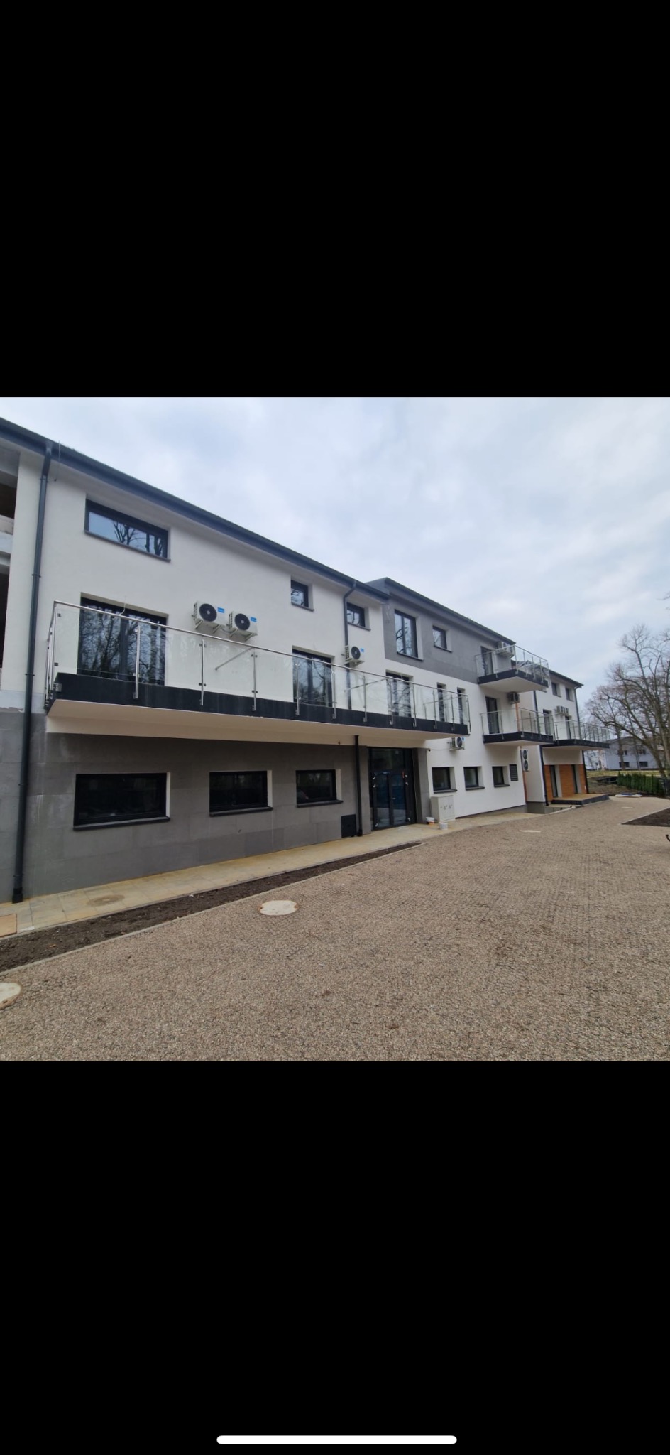 Nowoczesny budynek mieszkalny z balkonami zabezpieczonymi szklanymi balustradami i metalowymi poręczami, widoczne klimatyzatory na elewacji.