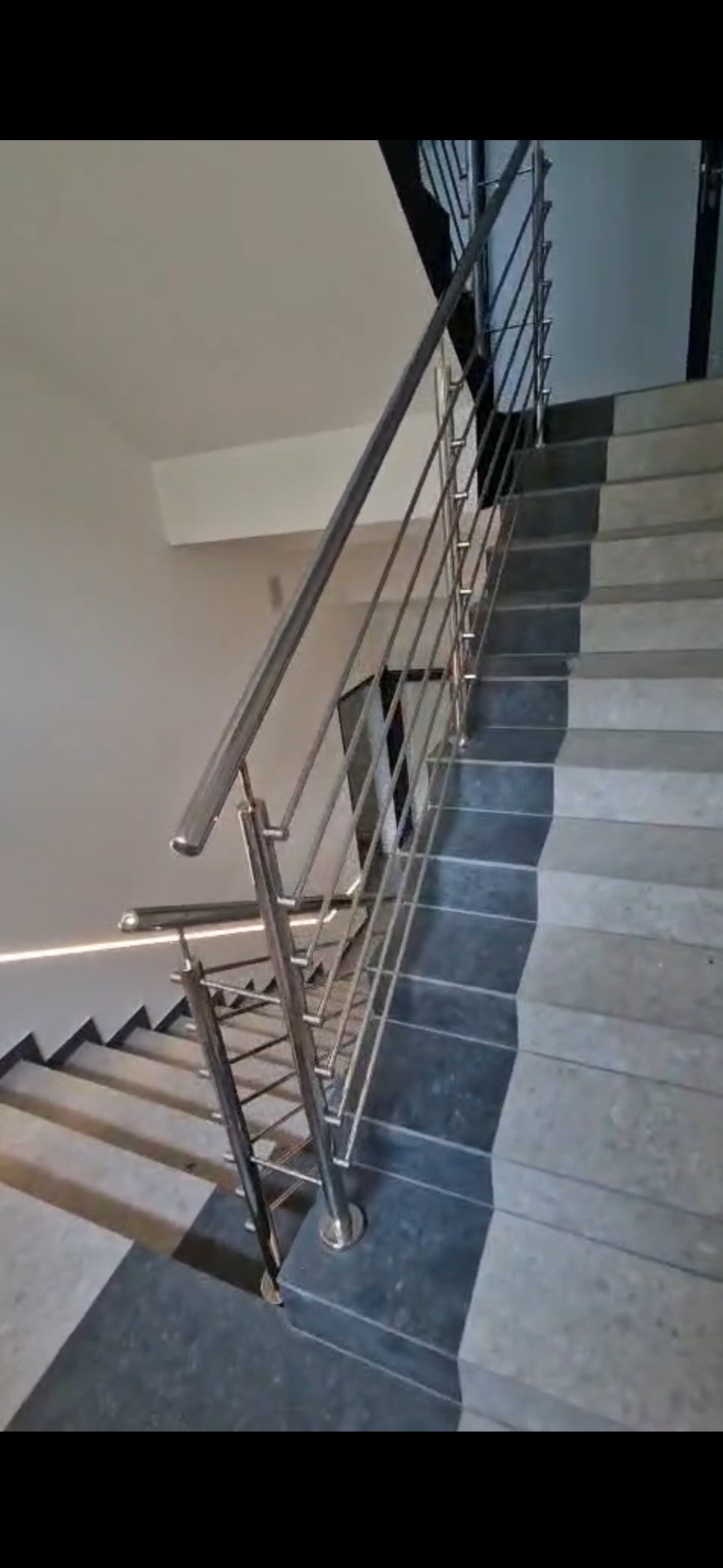 Wewnętrzne schody z szarymi stopniami i nowoczesną balustradą ze stali nierdzewnej z poziomymi prętami, oświetlenie LED pod schodami.