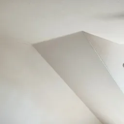 Fragment wykończonego narożnika sufitu pod skosem, gładka, jasna powierzchnia, widoczne łączenie płyt kartonowo-gipsowych.