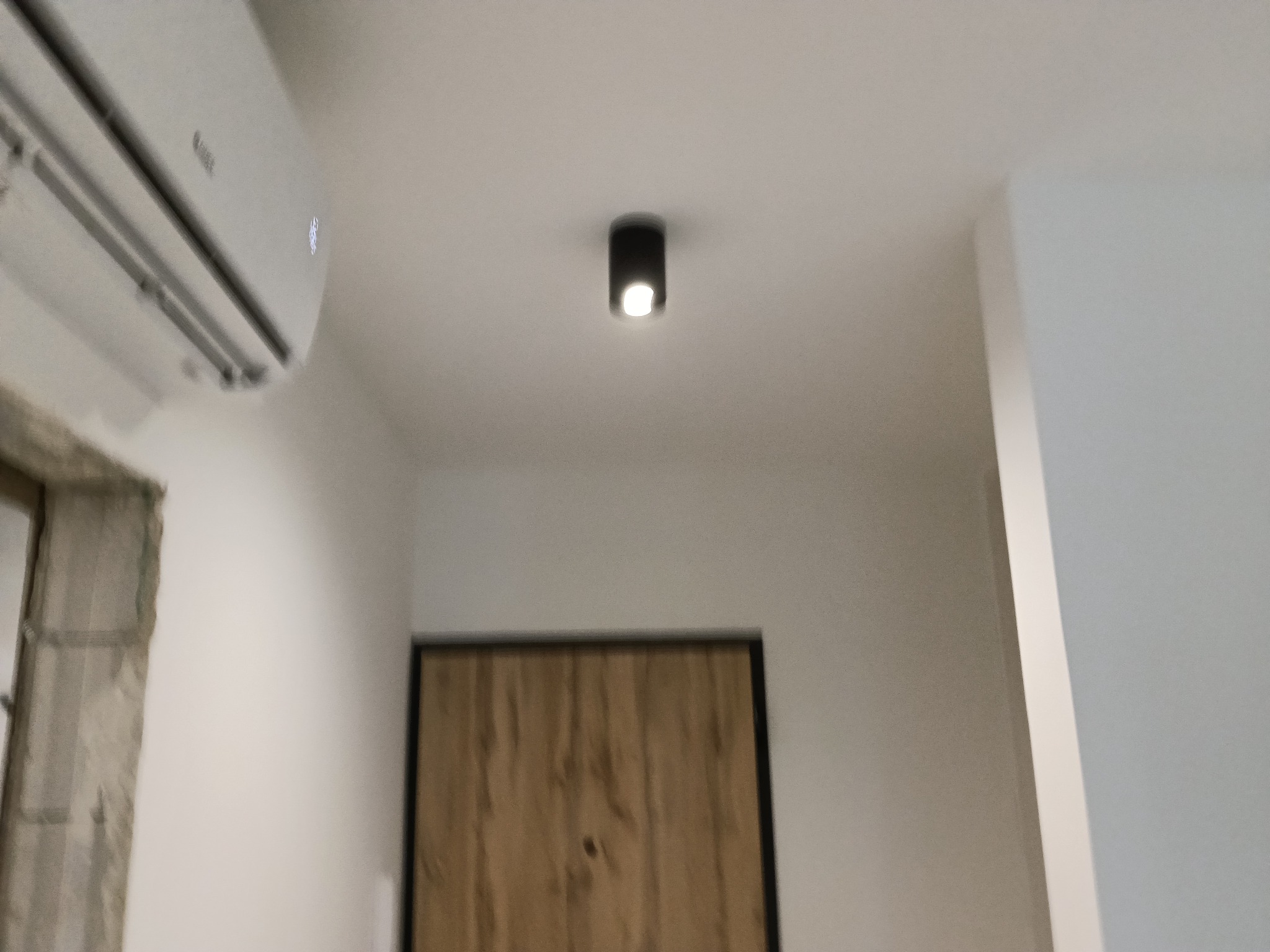 Wnętrze po remoncie: klimatyzator, sufitowa lampa punktowa i drzwi z drewnianą okleiną. Widoczny fragment okna z zasłoniętą szybą. Świeżo pomalowane ściany w jasnych odcieniach.
