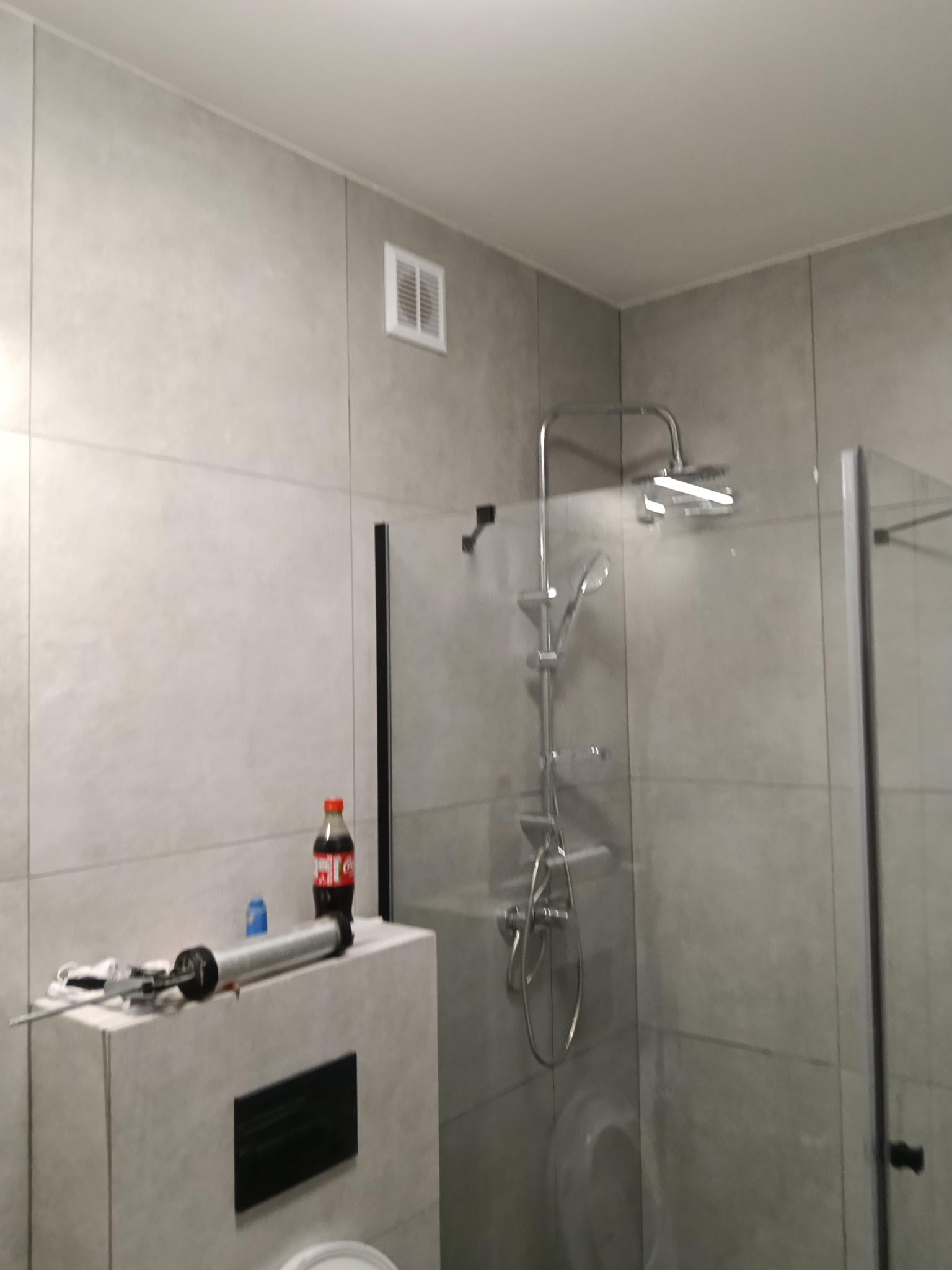 Wykończona łazienka z szarą glazurą, kabiną prysznicową typu walk-in i narzędziami do silikonowania. Widoczny wentylator sufitowy.