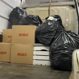 Wnętrze busa załadowane czarnymi workami na śmieci i kartonami OBI, przygotowane do transportu.