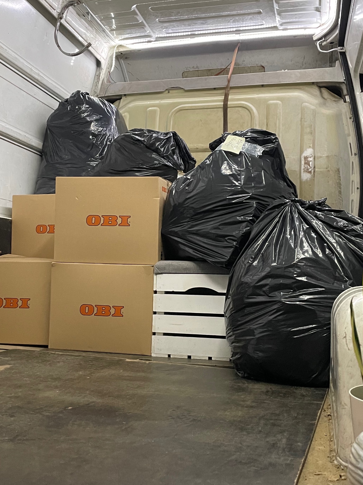 Wnętrze busa załadowane czarnymi workami na śmieci i kartonami OBI, przygotowane do transportu.