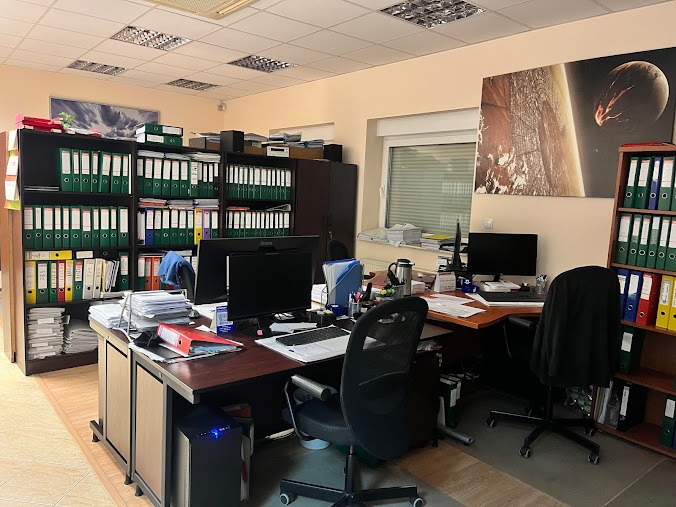 Biuro z dwoma stanowiskami pracy, regały wypełnione segregatorami, na ścianie grafika przedstawiająca kosmos.