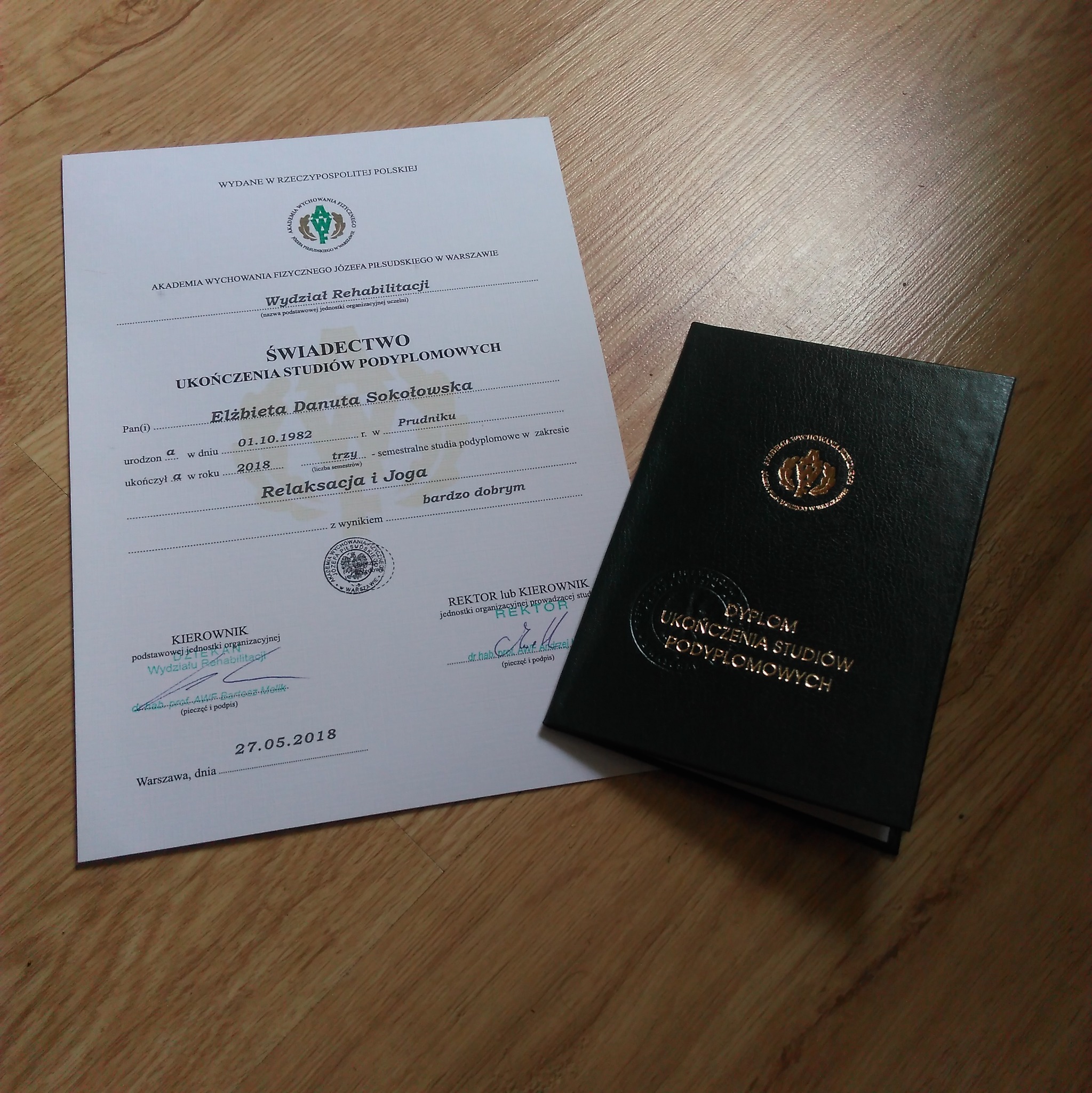 Świadectwo ukończenia studiów podyplomowych z zakresu Relaksacji i Jogi, wydane przez Akademię Wychowania Fizycznego Józefa Piłsudskiego w Warszawie, obok dyplom w ciemnozielonej oprawie ze złotym...