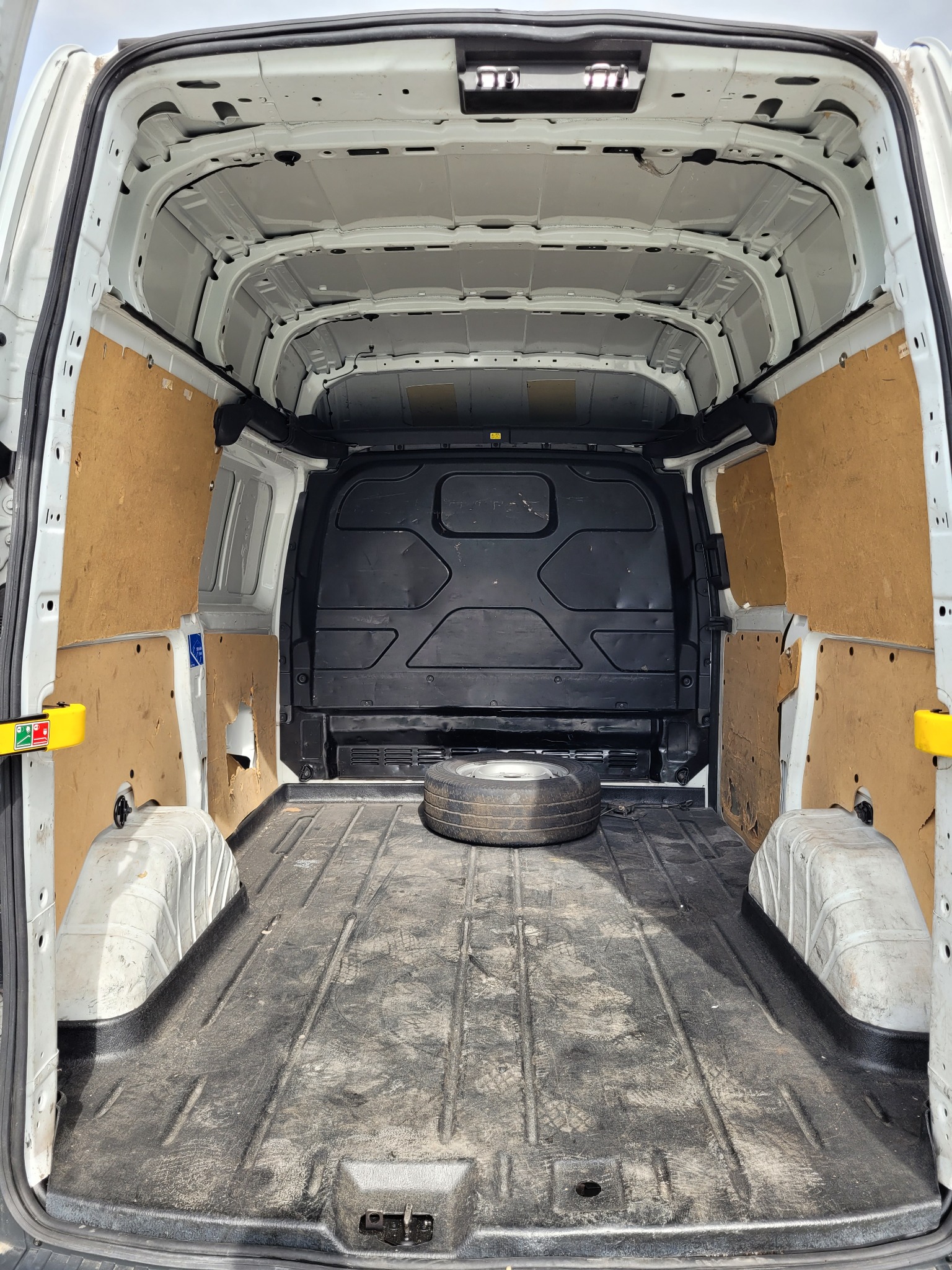 Wnętrze pustej furgonetki z zabezpieczonymi ścianami i kołem zapasowym na podłodze, widok z tyłu pojazdu.
