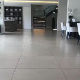 Szare, wielkoformatowe płytki podłogowe w przestronnym, nowoczesnym holu z widocznymi schodami i elementami dekoracyjnymi.