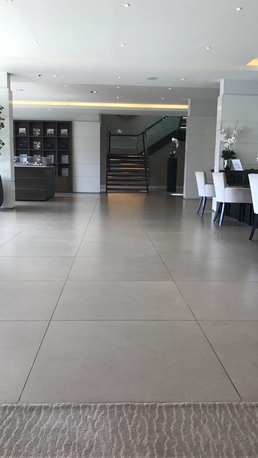 Szare, wielkoformatowe płytki podłogowe w przestronnym, nowoczesnym holu z widocznymi schodami i elementami dekoracyjnymi.