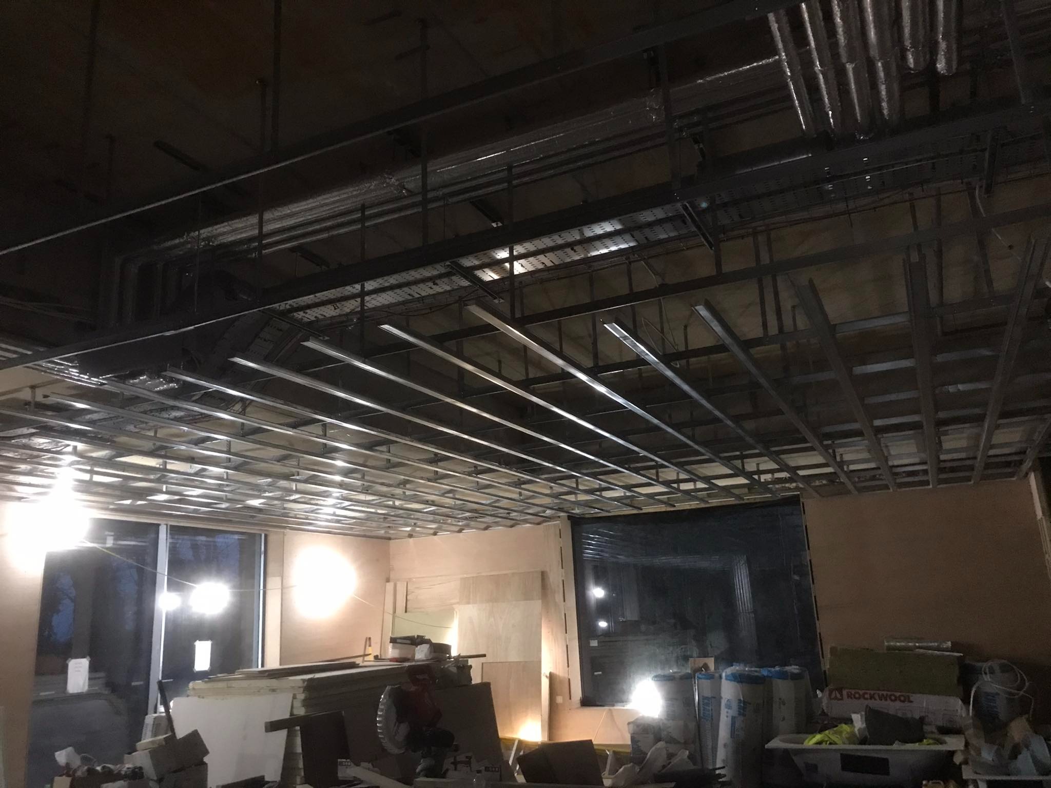 Montaż metalowej konstrukcji sufitu podwieszanego w pomieszczeniu w trakcie remontu, widoczne instalacje, materiały budowlane i izolacyjne Rockwool.