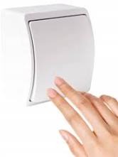 Dłoń naciskająca biały, zaokrąglony włącznik światła na białej ścianie, widok z bliska.