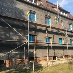 STAM - Budynek wielorodzinny w trakcie ocieplania, widoczne rusztowania, styropian na elewacji i okna zabezpieczone folią.