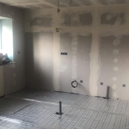 STAM - Wnętrze w trakcie remontu: ściany przygotowane do malowania, z widocznymi śladami szpachlowania i płyt karton-gips, na podłodze rozłożona folia z siatką pod ogrzewanie podłogowe, wystające rury...