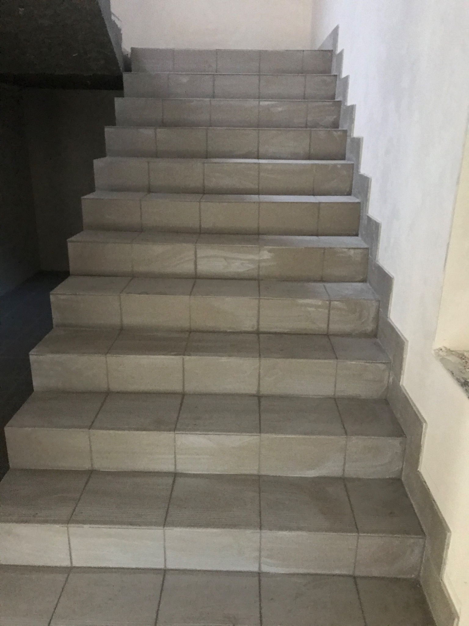 Schody wyłożone szarymi, kwadratowymi płytkami ceramicznymi, widok z dołu, ściana pomalowana na biało po prawej stronie.