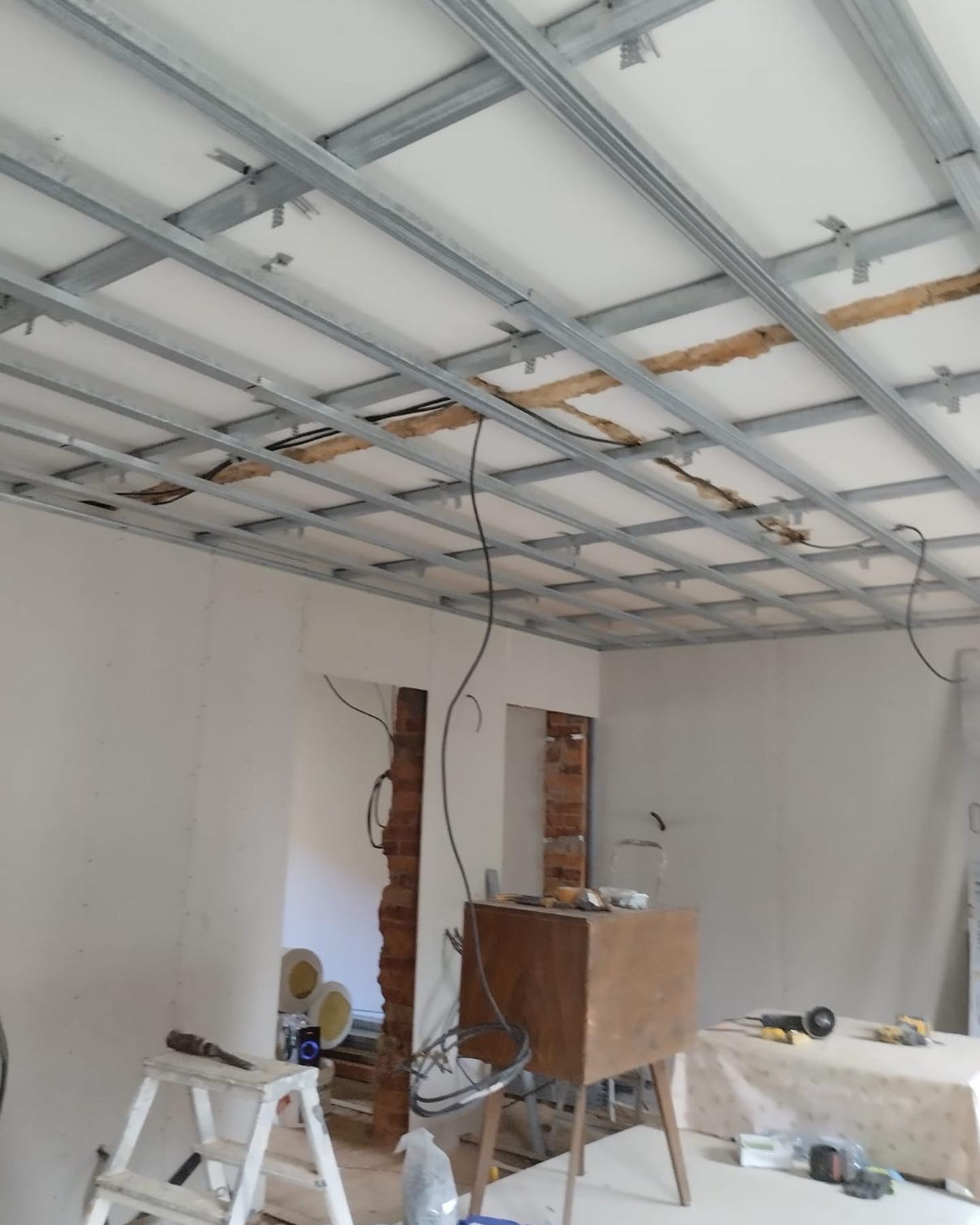 Montaż metalowego stelażu pod płyty gipsowo-kartonowe na suficie w trakcie remontu, widoczne kable i narzędzia.