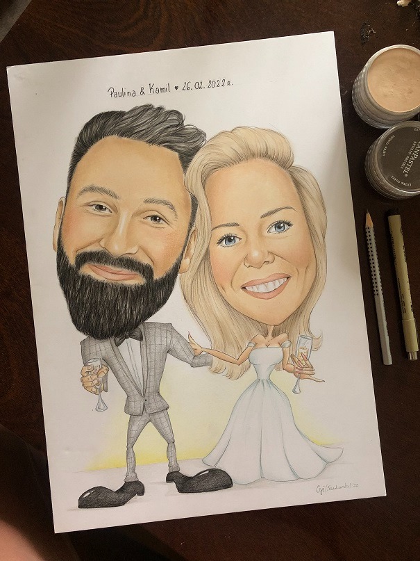 Ręcznie rysowana karykatura ślubna pary, Pauliny i Kamila, z datą 26.02.2022, z pastelami i ołówkami obok.