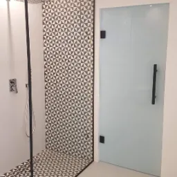 Nowoczesna kabina prysznicowa z czarną ramą i geometrycznym wzorem płytek, szklane drzwi z czarnym uchwytem, minimalistyczna armatura.