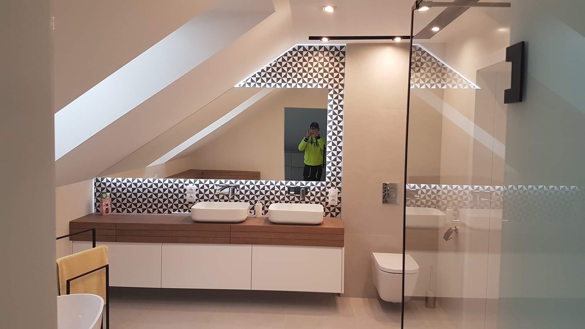 Nowoczesna łazienka na poddaszu z dwoma umywalkami nablatowymi, mozaiką w geometryczne wzory nad blatem i lustrem z podświetleniem LED, kabina prysznicowa ze szklanymi drzwiami.