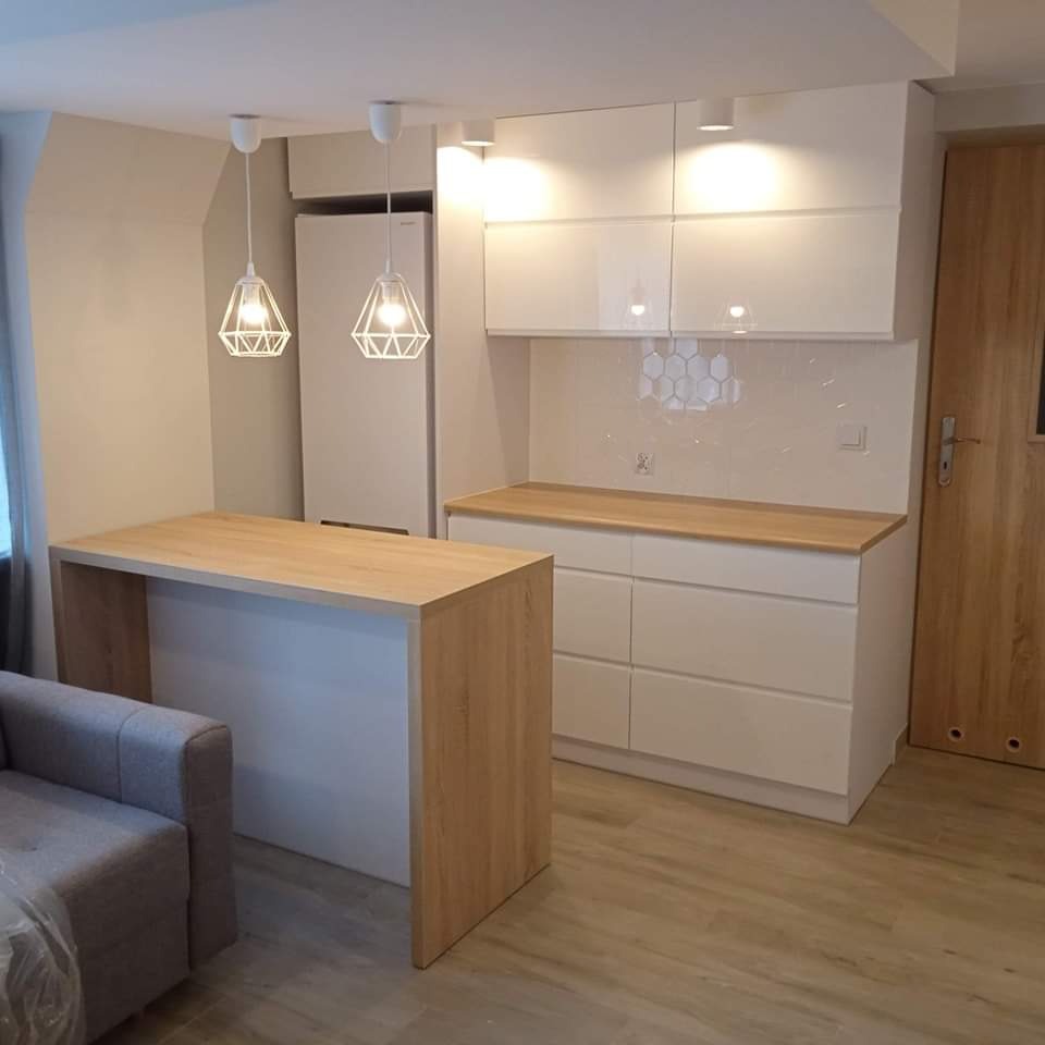 Nowoczesna, minimalistyczna kuchnia z białymi, lakierowanymi frontami szafek, drewnianym blatem i wyspą kuchenną z drewnianym wykończeniem, oświetlona dwoma designerskimi lampami wiszącymi...