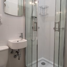Service4You - Nowoczesna, mała łazienka z narożną kabiną prysznicową z chromowanymi profilami, podwieszaną umywalką i lustrem z oświetleniem punktowym, wykończona białymi płytkami i drewnopodobną podłogą.
