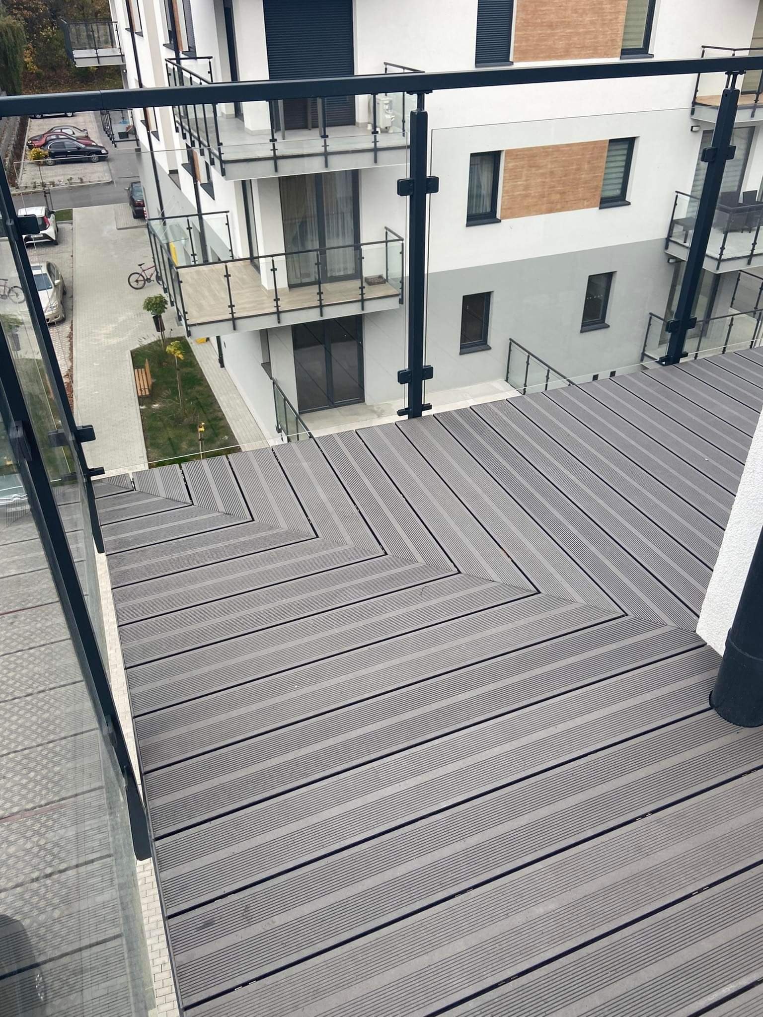 Szary, kompozytowy taras balkonowy z czarną balustradą szklaną, widok z góry na nowym budownictwie.