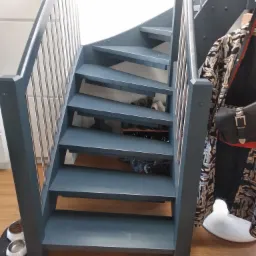 Nowoczesne, szare schody z metalowymi balustradami wewnątrz domu. Pod schodami widoczne buty i miski dla zwierząt.