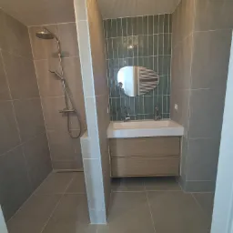 Nowoczesna łazienka z kabiną prysznicową i umywalką z szafką w Kielcach. Uwagę przykuwają zielone płytki nad umywalką i szara, duża płytka na podłodze i ścianach.