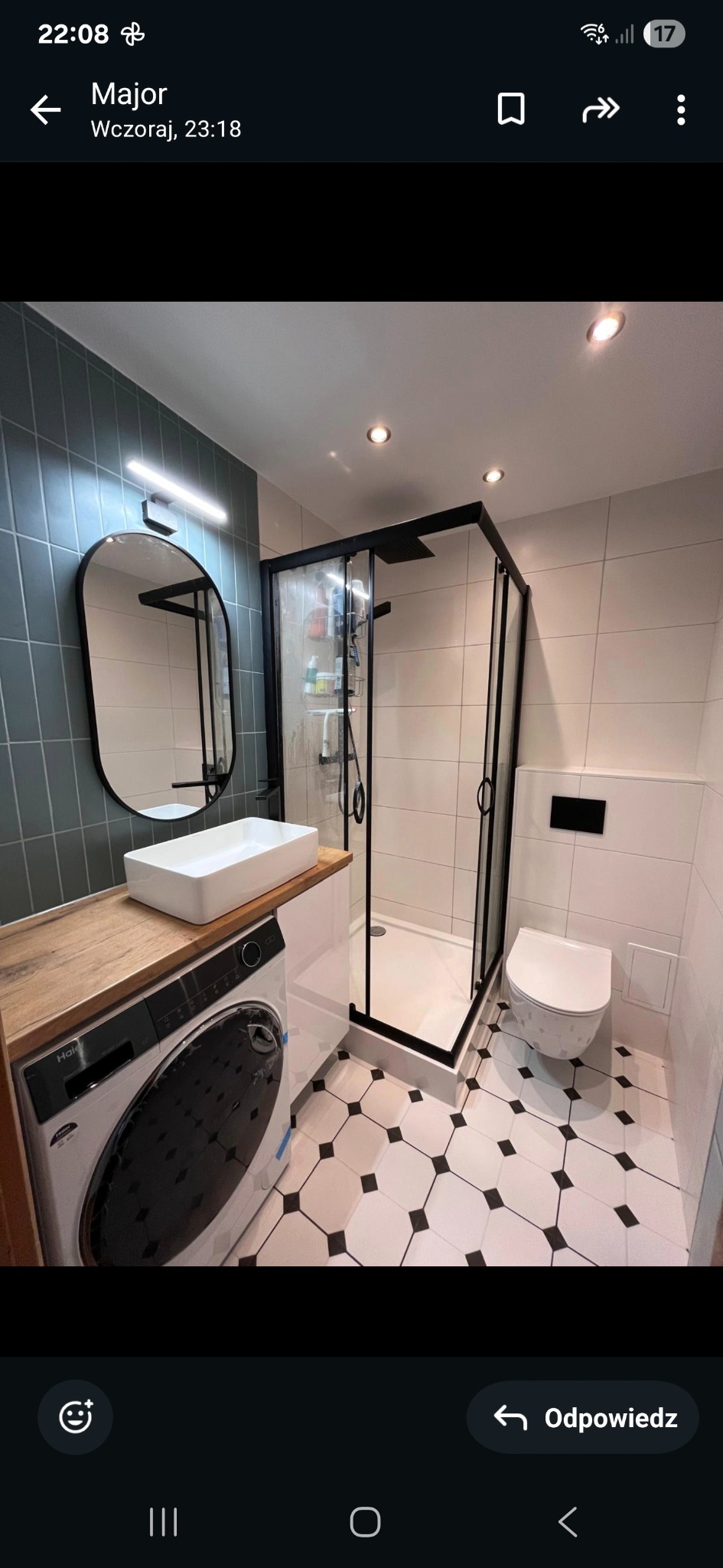 Nowoczesna łazienka z kabiną prysznicową typu walk-in, umywalką nablatową na drewnianym blacie nad pralką i biało-czarną podłogą w romby.