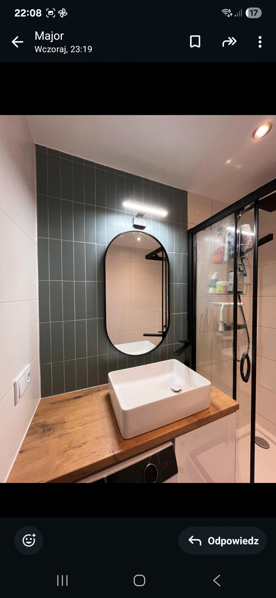 Nowoczesna łazienka: biała umywalka nablatowa na drewnianym blacie, grafitowe płytki na ścianie, czarna rama lustra i kabiny prysznicowej, minimalistyczny design.