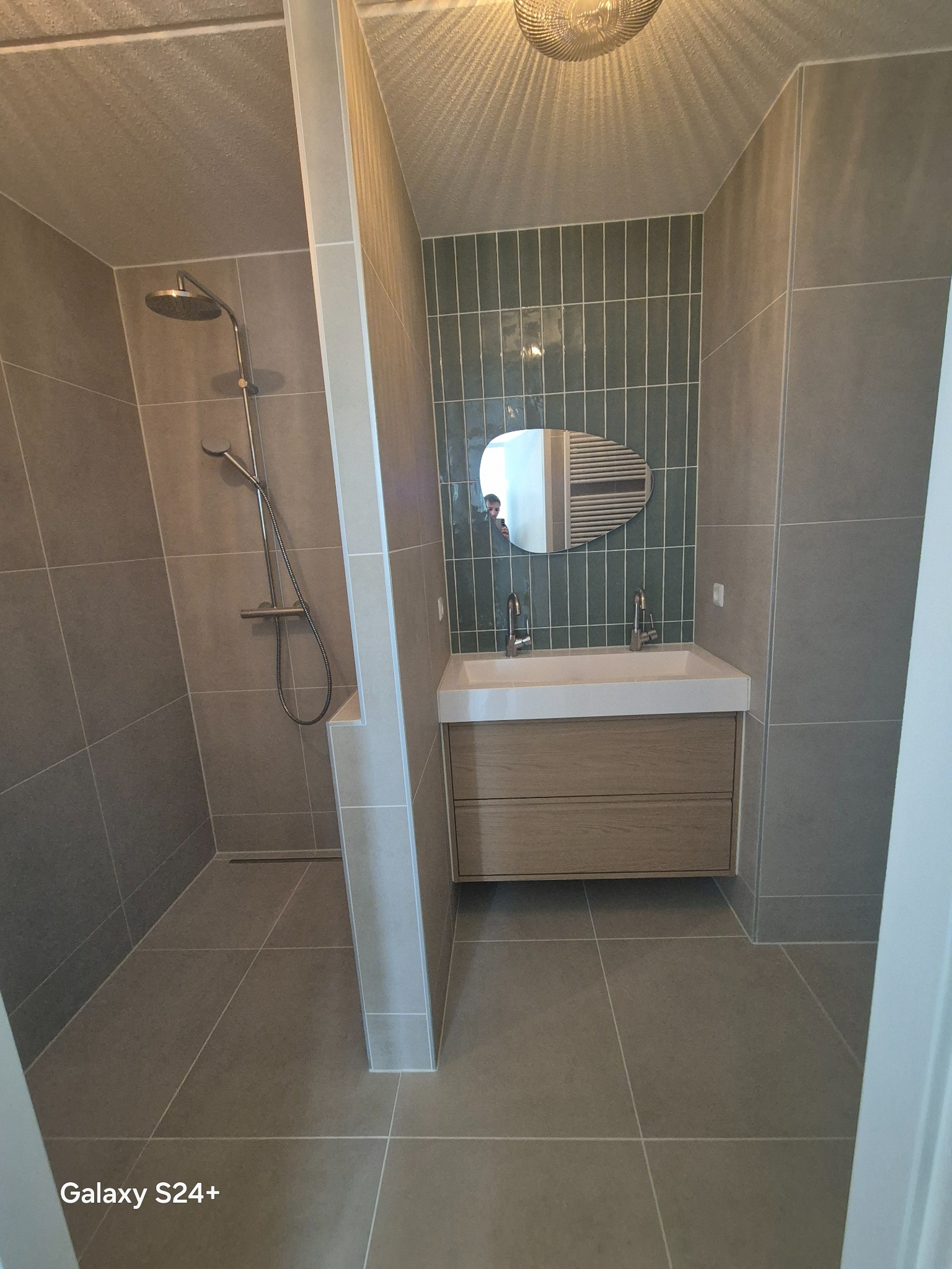 Nowoczesna łazienka z kabiną prysznicową i umywalką z szafką w Kielcach. Uwagę przykuwają zielone płytki nad umywalką i szara, duża płytka na podłodze i ścianach.